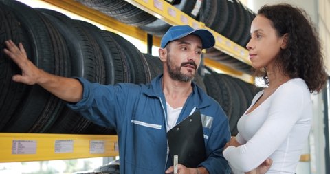 Salesman mechanics of tires talking about characteristic of product to customer came to look at assortment represented in auto service shop.