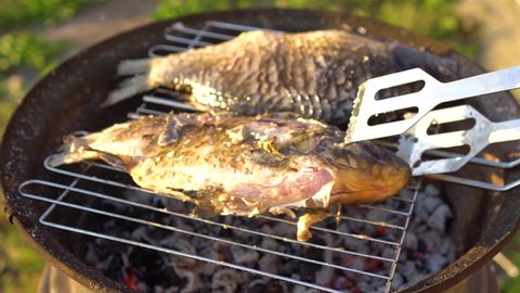The fish is fried on a grid and the chef takes care of the cooking. The chef puts the crucian carp on the grill. Fish is fried on the charcoal grill. Grilled dishes