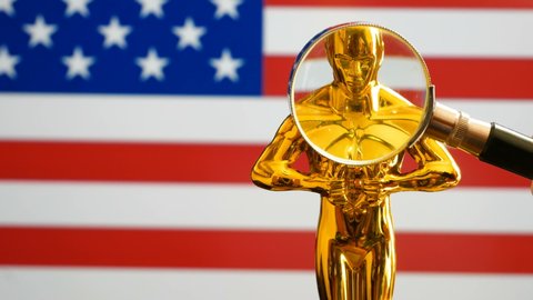 Hollywood Golden Oscar Academy award statue and magnifying glass
on american flag background. Success and victory concept.