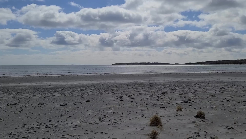 The waves rolling in at the beach off the coast of Nova Scotia, Canada. You can see the sand along the shore and the thickly wooded wilderness across the ocean on this beautiful partly cloudy day.