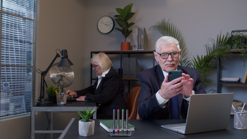 Senior professional businessman grandfather company director in modern office interior using mobile phone texing message working watching video successful people communicating. Elderly freelancer man Royalty-Free Stock Footage #1070410003