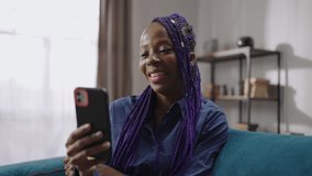 young afro-american woman is communicating with friends or family by video chat in modern smartphone, resting alone in weekend