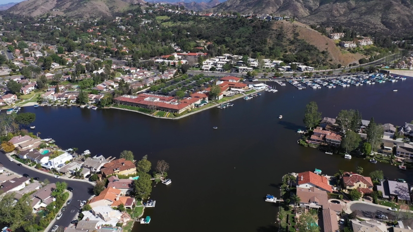 Westlake Village, California. Sunny Day at the Lake near The Landing overlooking scenic Restaurants and Boat filled Dock. Boats float near Lake View Real Estate from Aerial view. Royalty-Free Stock Footage #1070413513