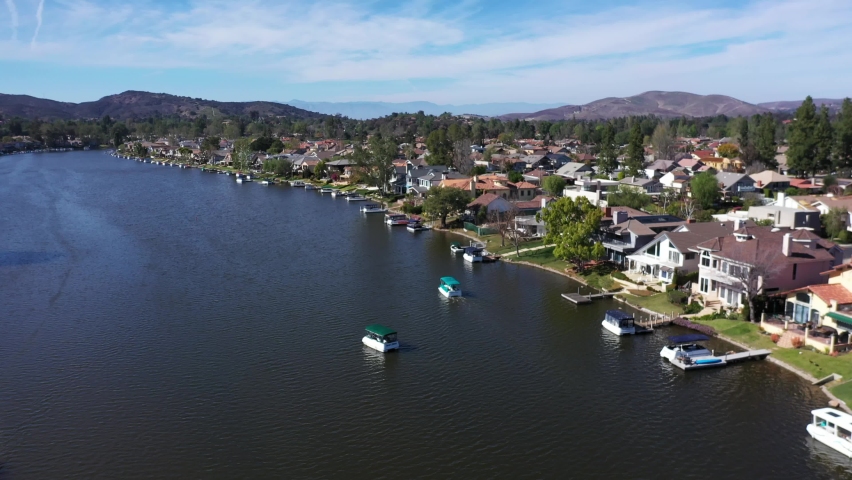 Westlake Village, California. Sunny Day at the Lake near The Landing overlooking scenic Restaurants and Boat filled Dock. Boats float near Lake View Real Estate from Aerial view. Royalty-Free Stock Footage #1070413531