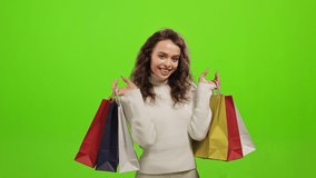 The woman is looking at the camera and smiling. She is picking up the shopping bags. She is standing on a green background. Green screen. 4K - Powered by Shutterstock - Get 15% off with code: PIKWIZARD15