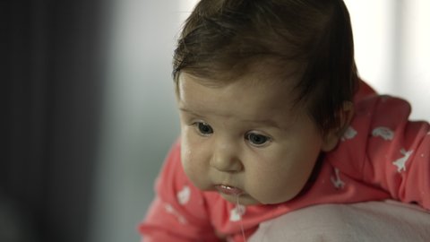 Little girl in mom's arms. The baby looks into the camera and saliva flows from her mouth. Beautiful video 4K slow motion of a child's life at home with parents.