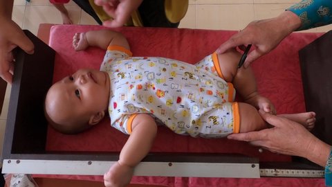 An adorable happy calm cute chubby big large healthy fat four month old asian baby boy is lie down and put in a manual height meter for health check by his mother at community healthcare services.