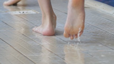 close-up of the feet of children in the pool, who step on the tiled floor with water and spray water to the side. Teenage swimmers' feet walk across the wet tiles of the pool. Slow motion