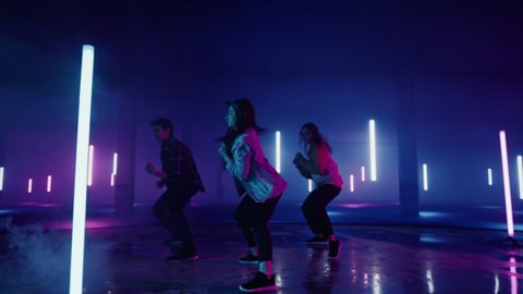 Diverse Group of Three Stylish Professional Dancers Performing a Hip Hop Dance Routine in Virtual Production Studio Environment with 3D Underground Garage Space with Neon Light Lamps. วิดีโอสต็อก