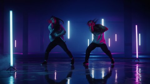 Two Stylish Professional Female Dancers Performing a Hip Hop Dance Routine in Virtual Production Studio Environment with 3D Underground Garage Space with Neon Light Lamps. Adlı Stok Video