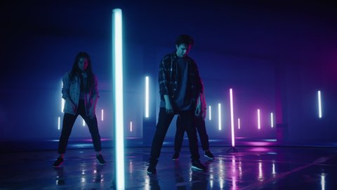 Diverse Group of Three Stylish Professional Dancers Performing a Hip Hop Dance Routine in Virtual Production Studio Environment with 3D Underground Garage Space with Neon Light Lamps.