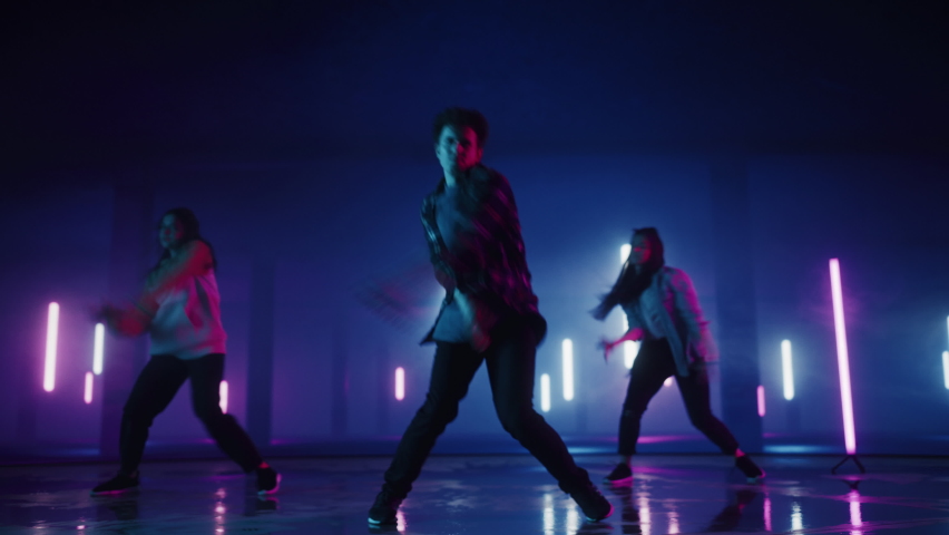 Diverse Group of Three Stylish Professional Dancers Performing a Hip Hop Dance Routine in Virtual Production Studio Environment with 3D Underground Garage Space with Neon Light Lamps. | Shutterstock HD Video #1070417827