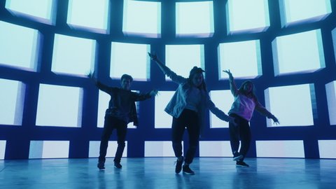 Diverse Group of Three Professional Dancers Performing a Hip Hop Dance Routine in Front of Big Led Wall Screen with Blue VFX Animation During a Virtual Production in Studio Environment. 105 BPM Song.