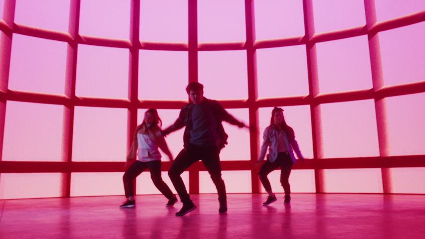 Diverse Group of Three Professional Dancers Performing a Hip Hop Dance Routine in Front of Big Led Wall Screen with Red VFX Animation During a Virtual Production in Studio Environment. 105 BPM Song. Royalty-Free Stock Footage #1070417941