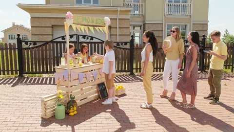 Full shot of people standing in queue to buy homemade lemonade from childs stand on hot summer day