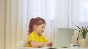 Little cute girl uses a laptop. The child looks into the frame and laughs. Children learn online through a computer. education internet online technology play beautiful caucasian child childhood.