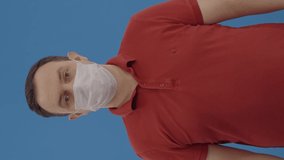 The man shows that taking off the mask is inconvenient.Indoor studio shot isolated on blue background. Slow motion video.Video for the vertical story.