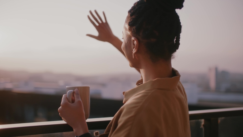Close up young african american woman stand on balcony looking out over city drinking a cup of tea or coffee touch sun. Relaxation,travel, interior, apartment. Slow motion