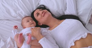 Portrait, a beautiful mother with a baby take a selfie and smile, they lie on a white bed. Young mother is talking to her child via a video call from a smartphone. Family values. 4k, ProRes