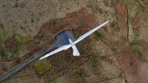 Top down aerial drone footage of large wind turbine with blades in field. Renewable energy and environmentally friendly concept. Cumbria, UK.