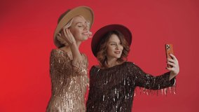 Two fashion bloggers girls make a selfie and send air kisses. Modern women communicate online. Video blog, call, message. Isolated on a red background.