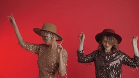 Two cheerful fashionable women wearing sequin dress are dancing at the party. Girls toss their hats up. Celebrating a birthday or new year. Isolated on a red background. - Powered by Shutterstock - Get 15% off with code: PIKWIZARD15