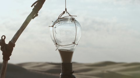 A stream of sand spilling out of a broken hourglass. Still life shot among the dunes in the desert. A hint of global problems: climate warming and environmental pollution. A symbol of fleeting life 