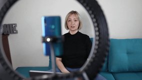 Video blogging. Business style woman talking to camera and recording video with smartphone and ring light lamp at home, working from home concept, social distant reality