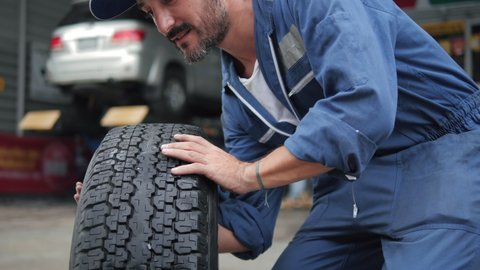 Portrait of male mechanic with car tire in auto store, Specialist tire fitting in the car service, checks the tire and rubber tread for safety.