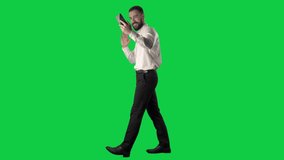 Side view of happy walking business man filming selfie videos greeting and winking. Full body on green screen chroma key background.