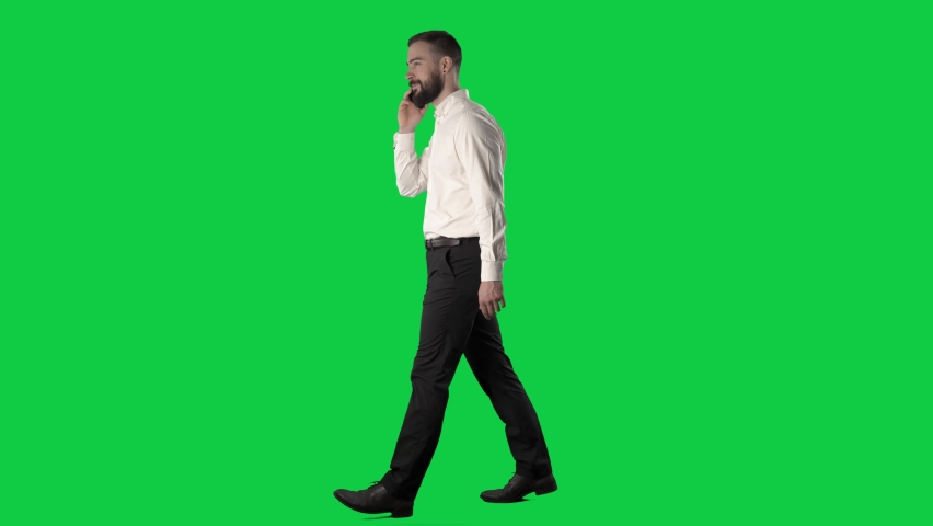 Side view of walking happy confident business man answer call and talking on the phone. Full body on green screen chroma key background.