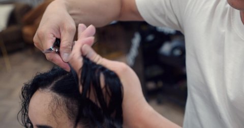 A young brunette woman in a beauty salon has a haircut in a barbershop, in a barbershop a man does a hairstyle for a brunette in a barbershop, a man hairdresser combs his hair. 4K slow motion.