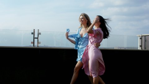 Sunny day in the roof top of loft apartment two charismatic large smile friends women in pajamas in the morning enjoying the moment and the city view