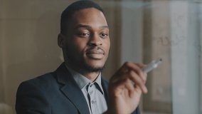 Portrait of focused afro american business man 30s executive manager writes formula financial calculations counting on transparent glass board, analyzes start-up, makes innovation, gets success result - Powered by Shutterstock - Get 15% off with code: PIKWIZARD15