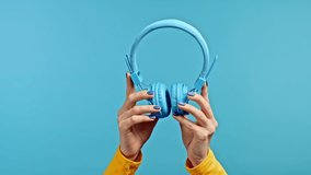 Hands of woman with wireless headphones isolated on blue studio background. Music, radio concept.
