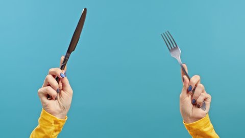 Hands of woman with fork and knife. Lady waiting for serving dinner dishes with cutlery on blue studio background. Only hands.