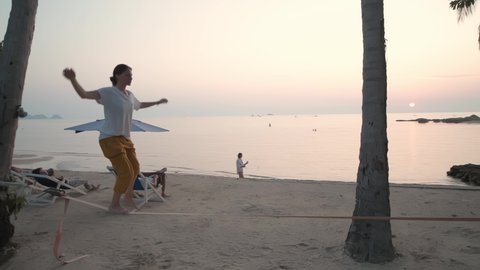 The girl goes on a slackline at sunset on a tropical beach. 