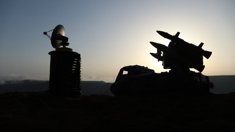 Creative artwork decoration. Silhouette of mobile air defence truck with radar antenna during sunset. Rocket launcher aimed at sky ready to attack. Selective focus