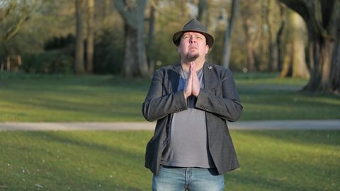 [4k] best ager goatee man wearing hat praying to god in park