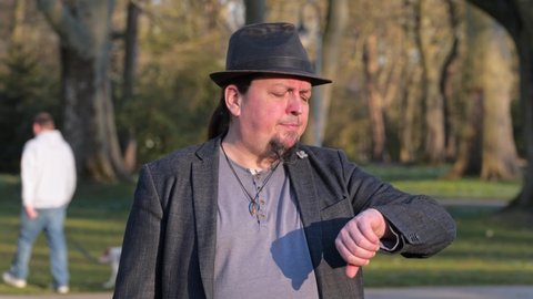[4k] annoyed goatee man wearing hat waiting for someone in public park