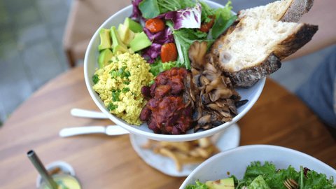 Hands presenting two vegan meals options of buddha bowl and a salad gto the camera. 