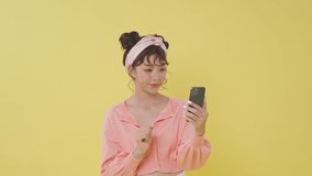 Young Asian woman using mobile phone doing selfie videoconference talk conducting pleasant conversation greet with hand isolated on yellow background.