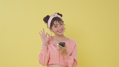 Excited beautiful young Asian woman using mobile phone typing browsing say wow yes just found out great big win news doing winner gesture isolated on yellow background.
