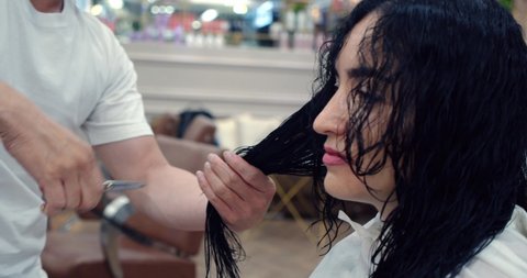 A young brunette woman in a beauty salon has a haircut in a barbershop, in a barbershop a man does a hairstyle for a brunette in a barbershop, a man hairdresser combs his hair. 4K slow motion.
