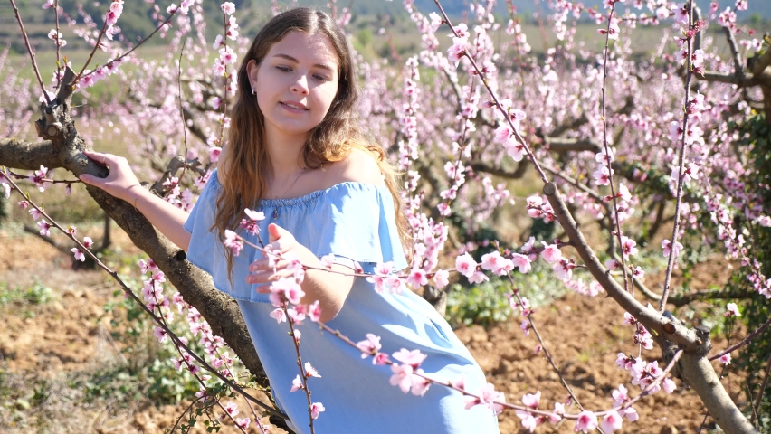 Young pretty american woman in blue dress posing in blossom spring garden