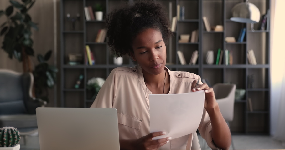 Happy beautiful young african american business lady working with paper documents, sitting at table with computer in modern home office. Smart skilled female biracial professional analyzing data. Royalty-Free Stock Footage #1070465977