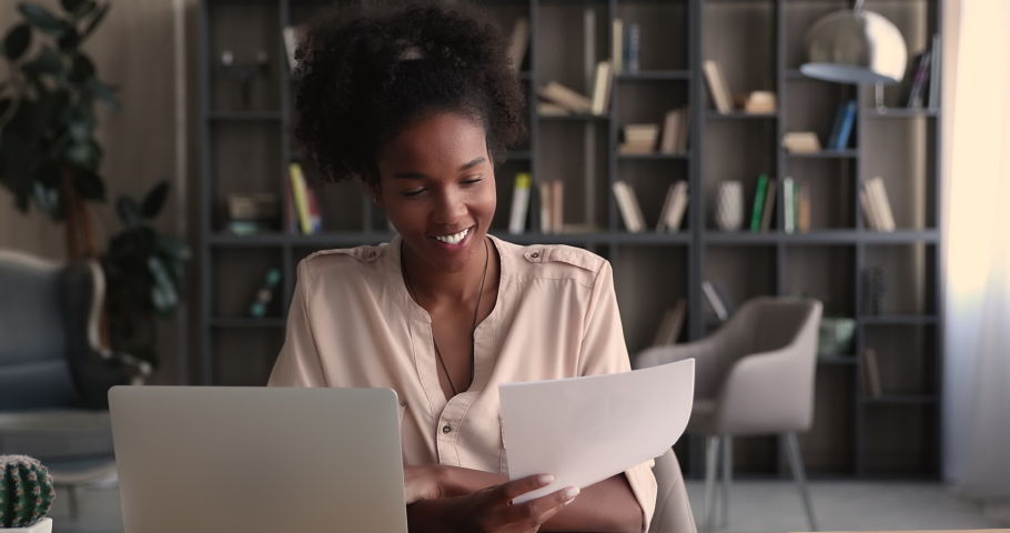 Happy beautiful young african american business lady working with paper documents, sitting at table with computer in modern home office. Smart skilled female biracial professional analyzing data. Royalty-Free Stock Footage #1070465977