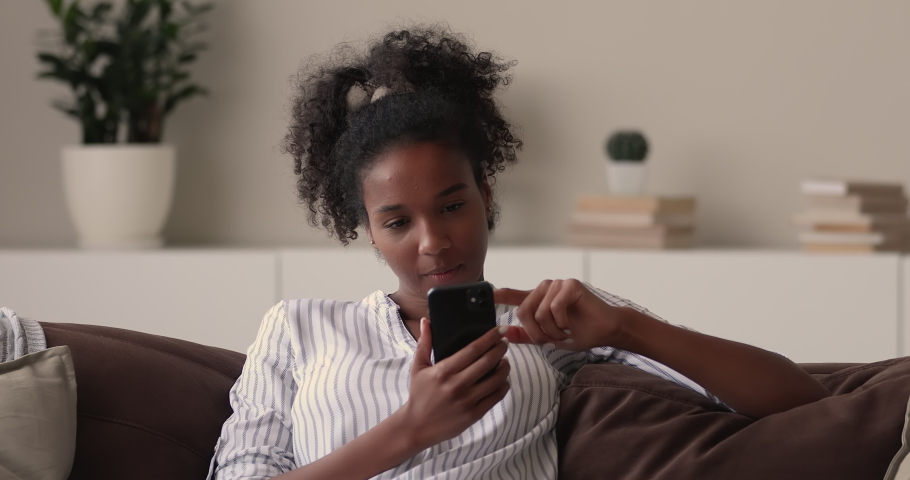 Smiling beautiful african ethnicity woman looking at telephone screen, reading message with good news, celebrating online lottery betting auction win or getting shopping promo code, internet success. Royalty-Free Stock Footage #1070466037