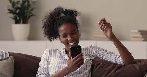 Smiling beautiful african ethnicity woman looking at telephone screen, reading message with good news, celebrating online lottery betting auction win or getting shopping promo code, internet success.