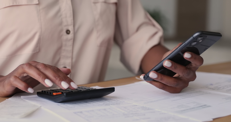 Close up young african mixed race woman using mobile e-banking application, checking paper bills, managing monthly household or personal budget, making payments online, calculating utilities. Royalty-Free Stock Footage #1070466100